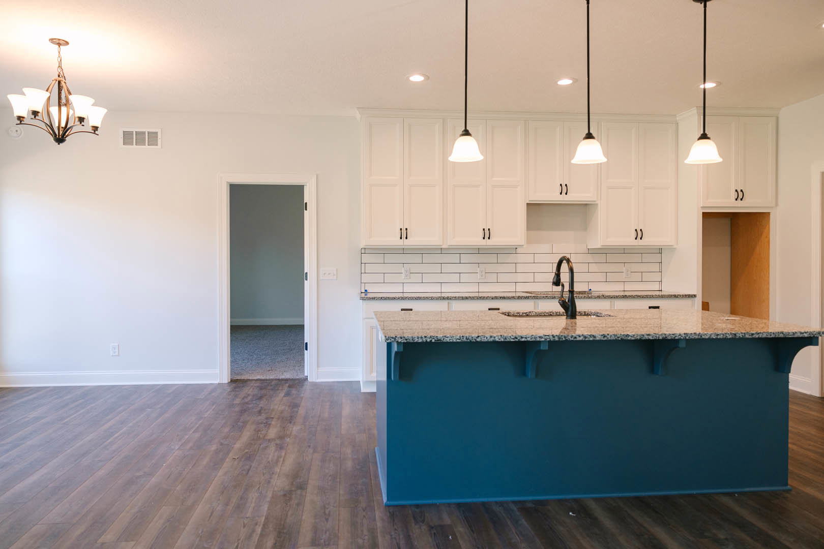 Blue kitchen island with granite countertop, white shaker cabinets, tile flooring, stainless steel sink, five-light chandelier, recessed ceiling light, blue accent wall with white