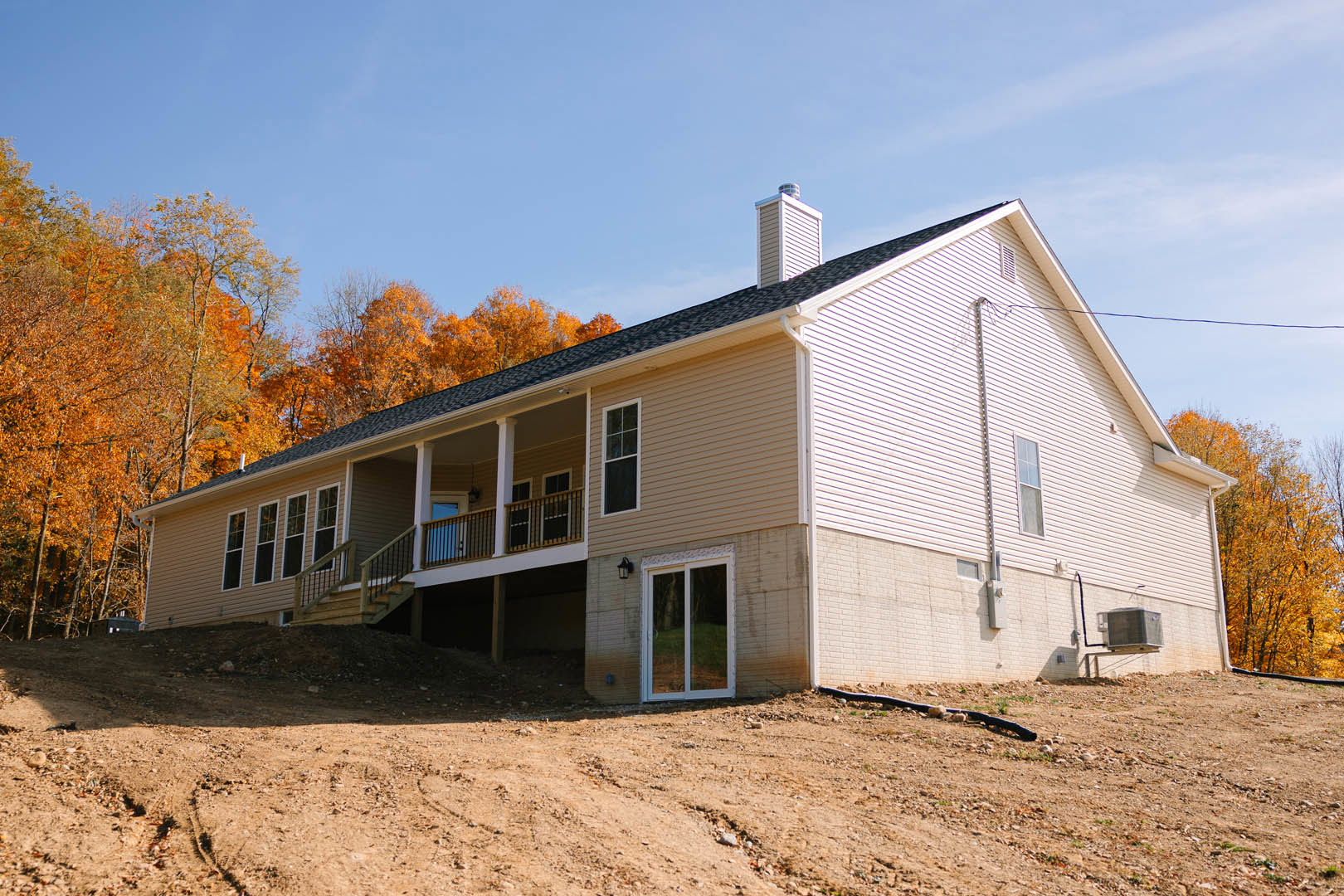 Two-story house with wide covered porch, white trim windows, wood siding, and a dirt hill in the foreground