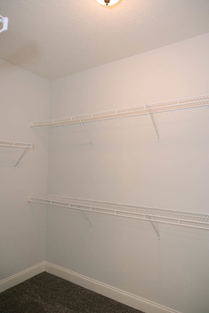 White built-in shelves on a plaster wall with a close-up of light carpet flooring, white metal rod suspended from the ceiling, and a ladder partially visible in a foggy indoor