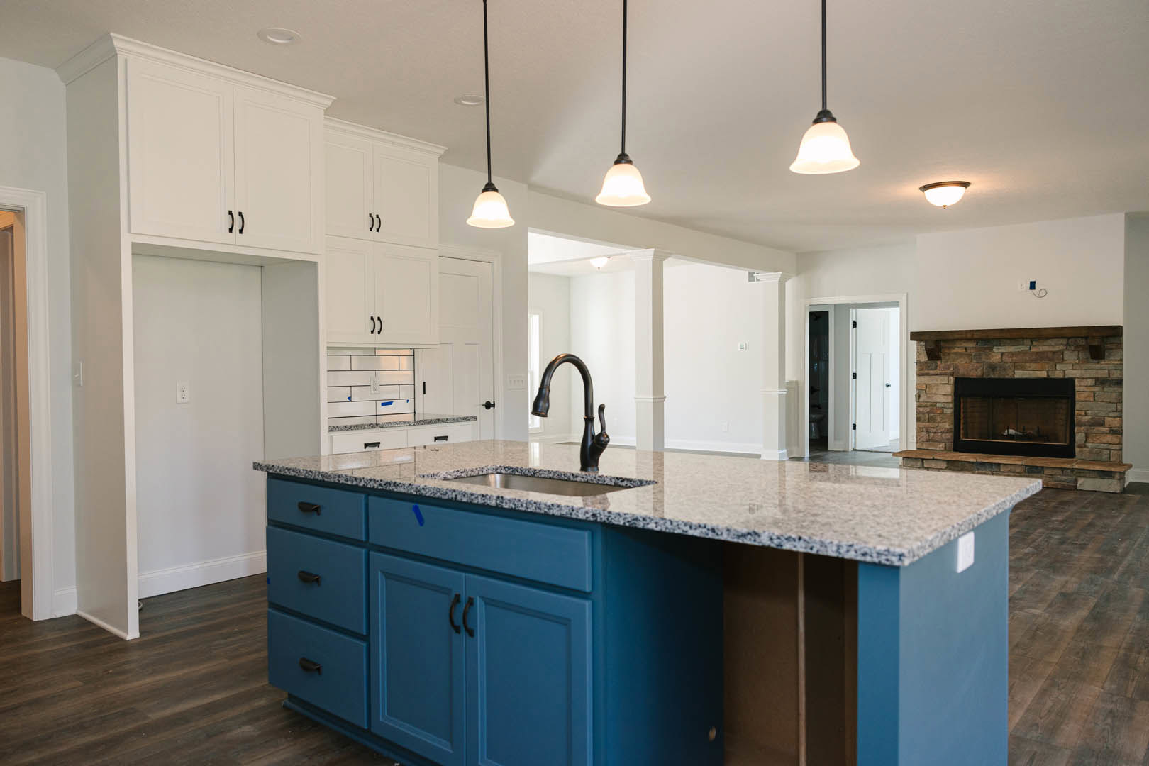 Spacious kitchen featuring a large central island with a white countertop, black curved faucet, built-in sink, glass-front cabinetry, tiled backsplash, fireplace with glass door