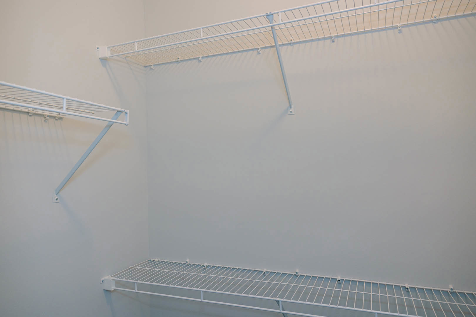 White shelving unit with metal rods mounted on a wall, white cloth draped over one shelf, set against a plain white background in a residential interior.