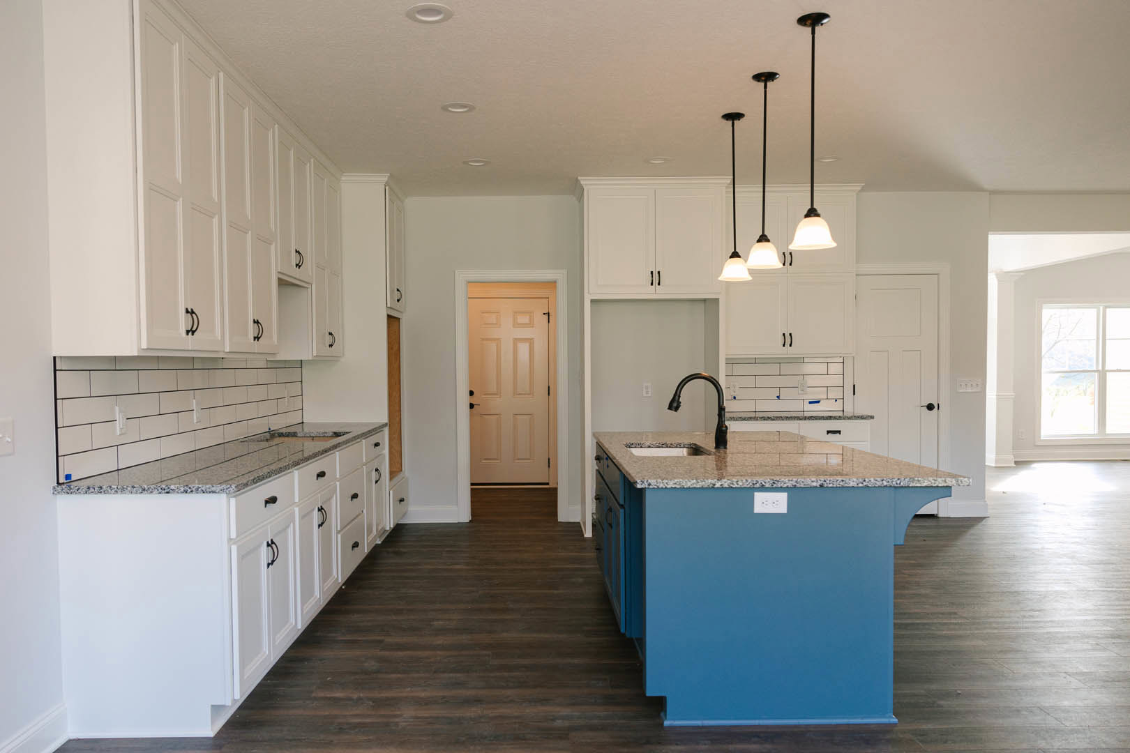 Blue kitchen island with built-in sink, surrounded by white shaker cabinets, tile backsplash, stainless steel appliances, and light wood flooring