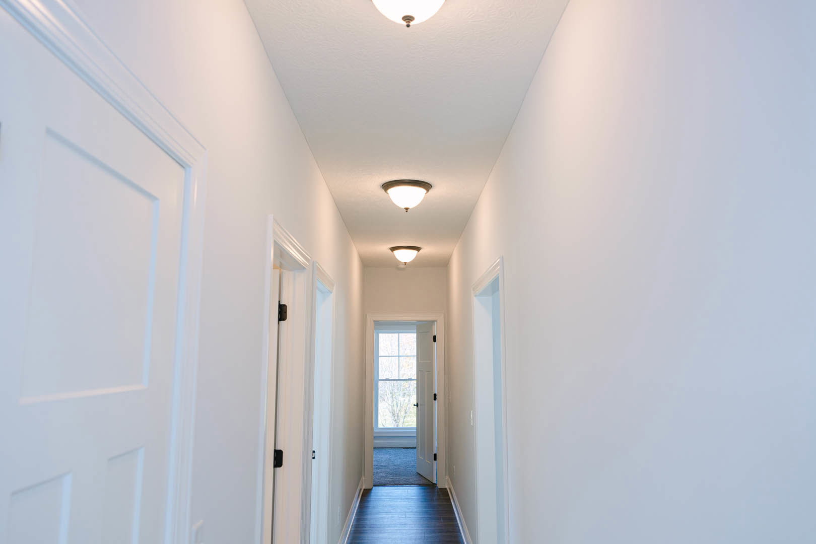 Hallway with white plaster walls, dark wood flooring, ceiling light fixture, white door with window, decorative molding