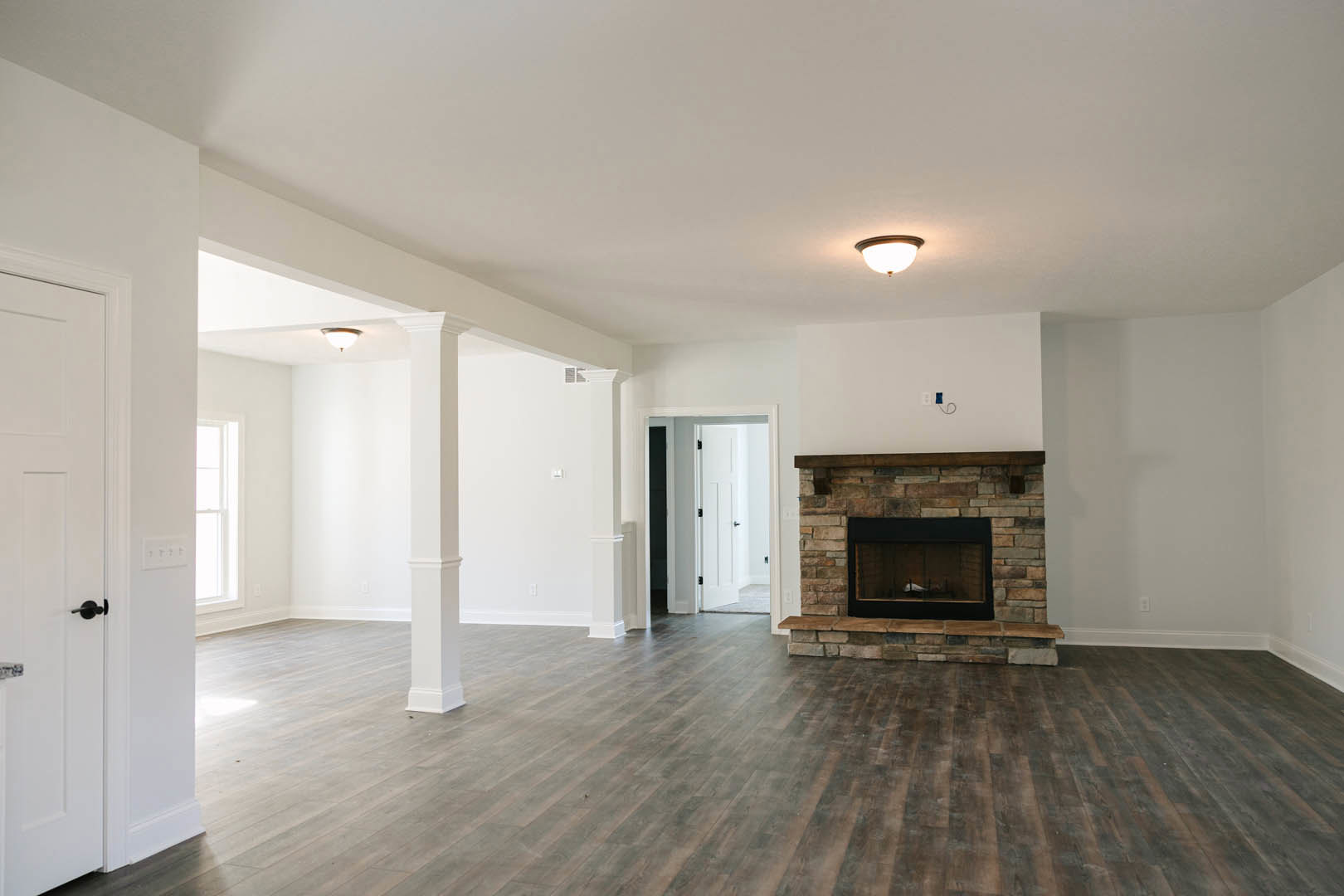 Living room with hardwood flooring, black-framed fireplace, white plaster walls, round ceiling light fixture, and doorway leading to adjacent space