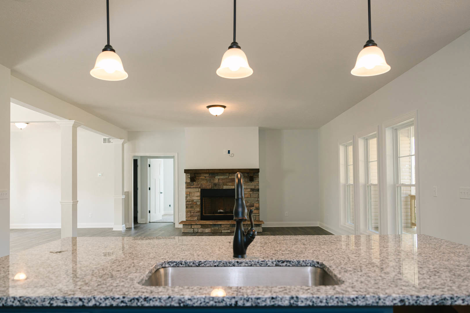 Granite countertop with black faucet and undermount sink, black-framed window above, white cabinetry, tile backsplash, and modern fireplace with black surround in open kitchen.