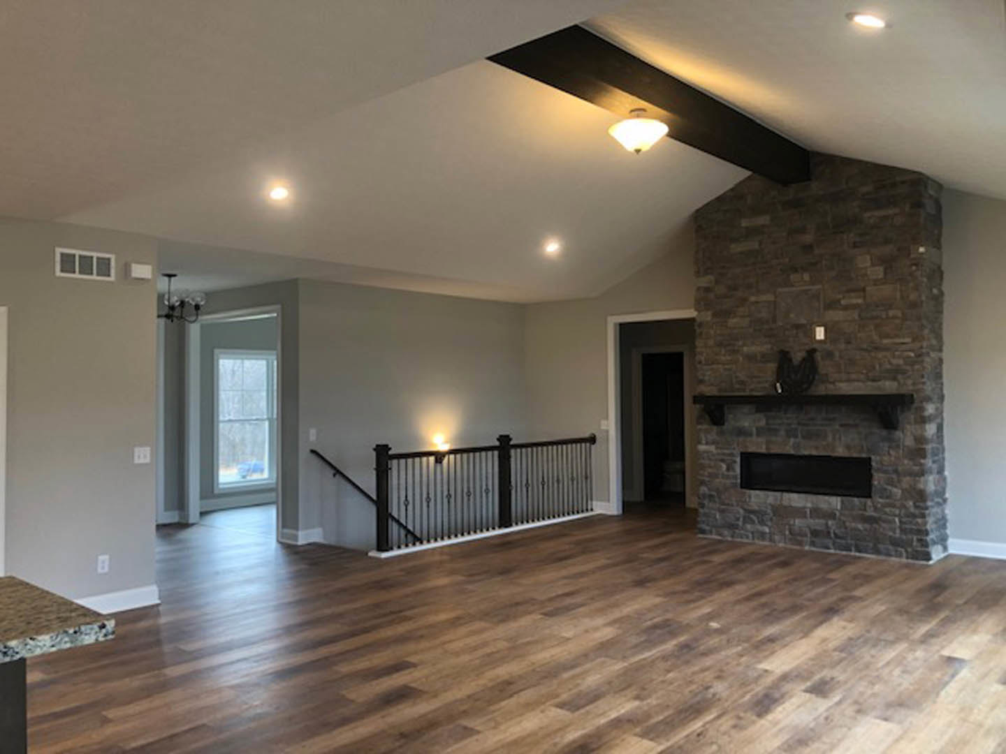 Living room featuring a stone fireplace with black mantel, wood flooring, black metal railing, wall-mounted light fixture, and white ceiling