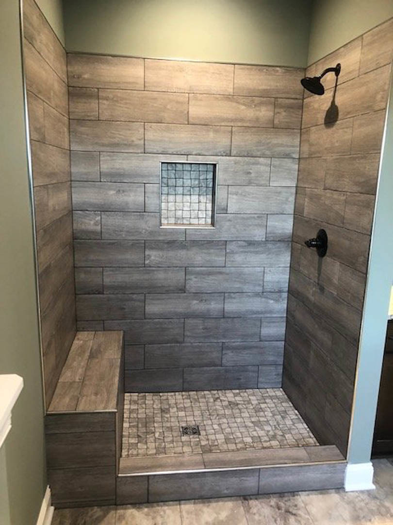 Walk-in shower featuring a built-in tile bench, marble tile walls and floor, linear drain, window, and black floor accent