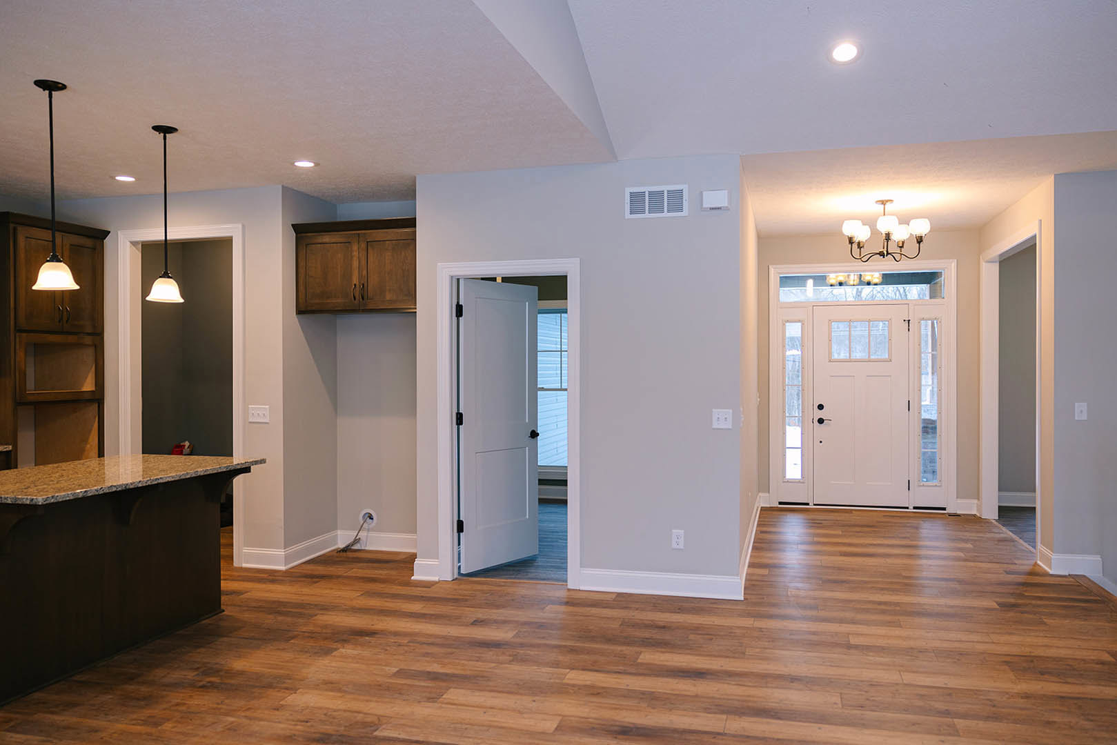 Open white door with glass panes leading to kitchen featuring wood laminate flooring, white cabinetry, stone countertop, and modern chandelier