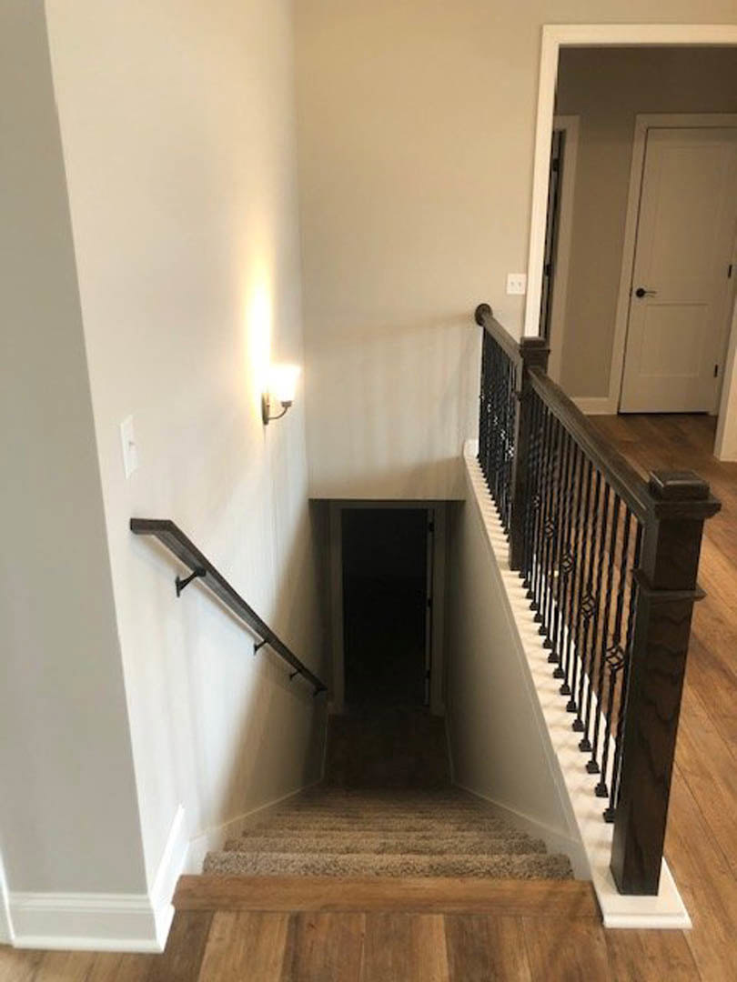 Hardwood staircase with white plaster walls, black metal handrail, open white door with black handle, and illuminated hallway beyond