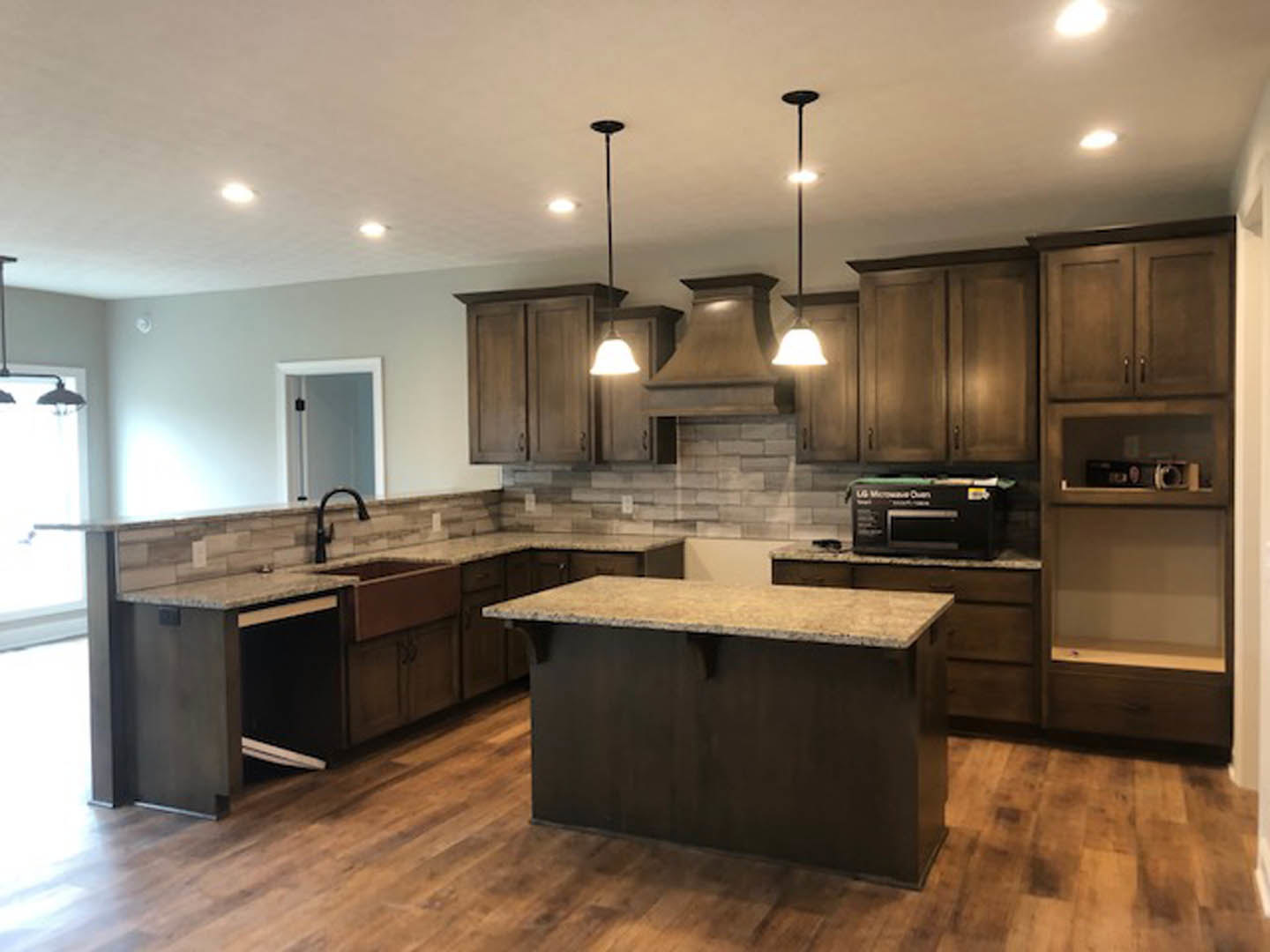 Open kitchen with natural wood flooring, white cabinetry, stone countertop, stainless steel appliances, and recessed lighting