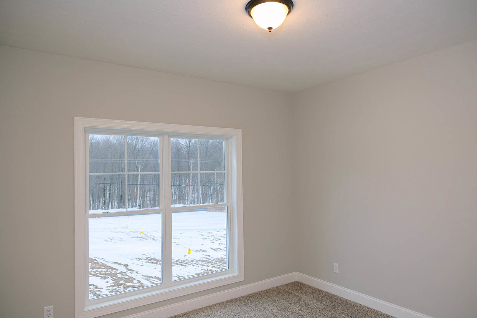Carpeted room with white walls, large window showing snowy landscape, round ceiling light fixture, and simple molding details