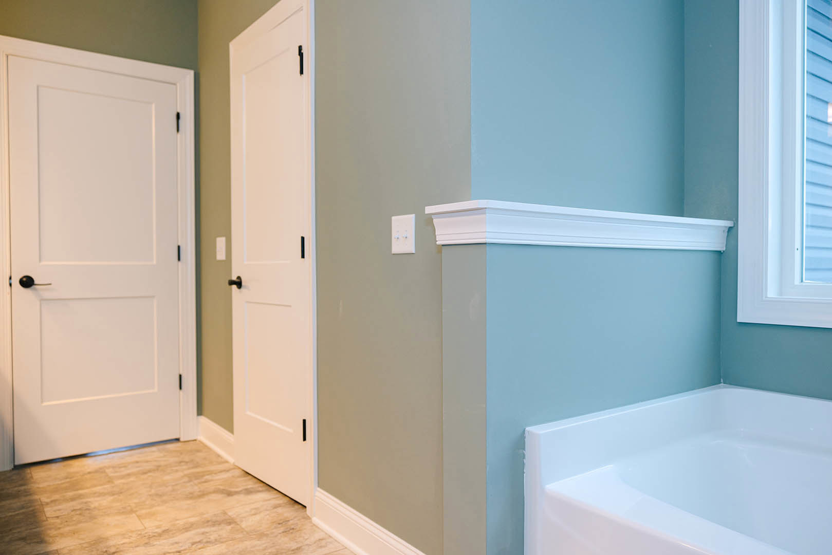 Bathroom featuring a freestanding white bathtub against a blue accent wall, white paneled doors with black handles, tile flooring, and a window allowing natural light.