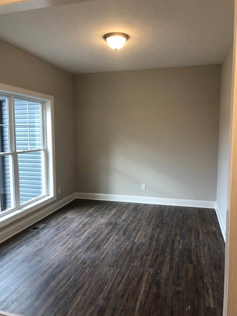 Dark hardwood floor in a room with white walls, large window, and modern ceiling light fixture