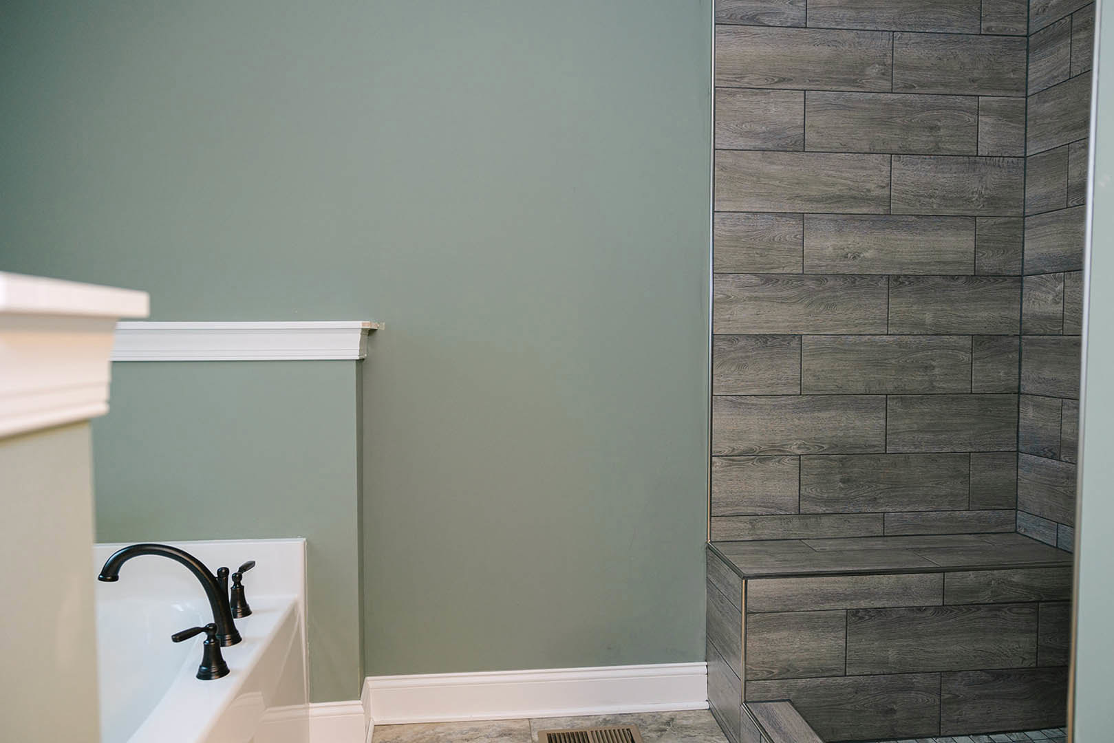 Bathroom with wood-look tile wall, built-in shelf, freestanding bathtub, chrome faucet, white sink, and white baseboard trim