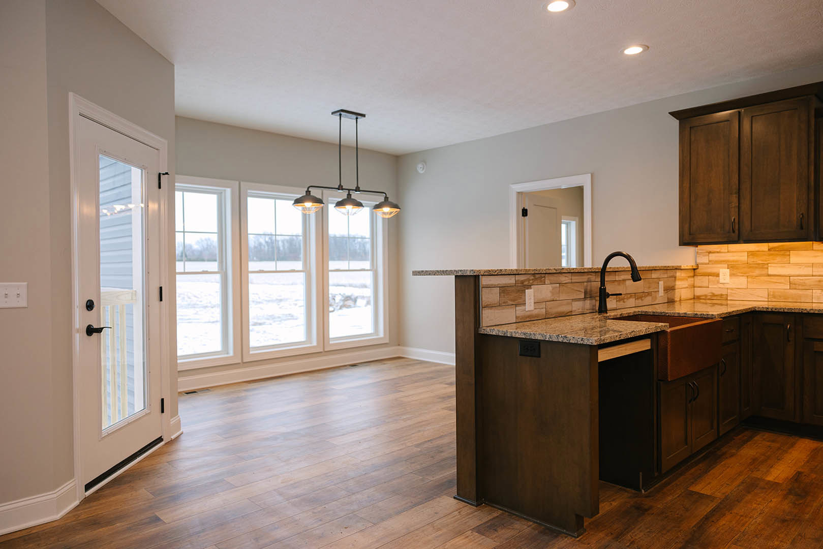 Kitchen with natural wood flooring, white cabinetry, black door handle, modern ceiling light fixture, stainless steel faucet, and close-up of a light switch on the wall