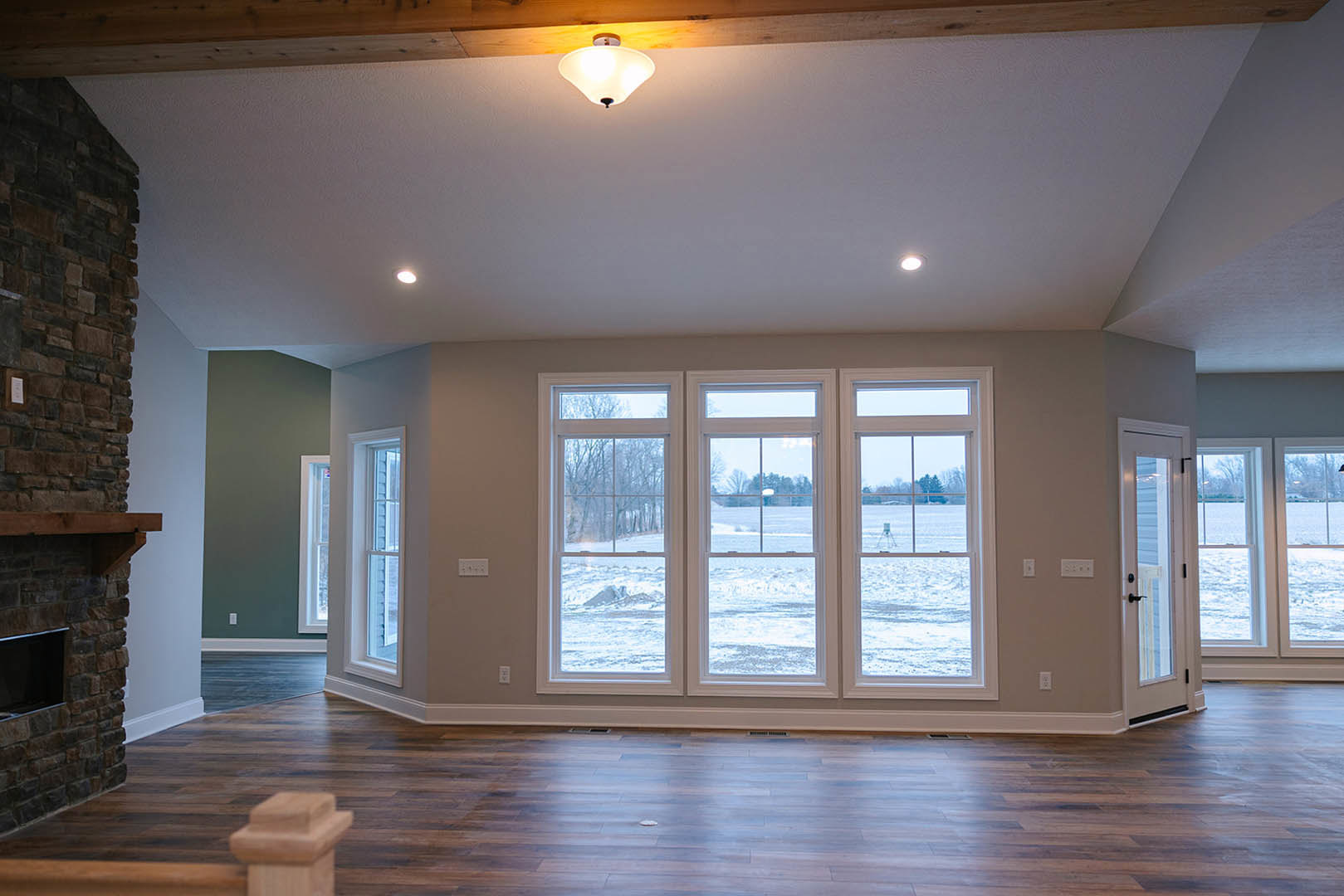 Spacious room featuring large windows overlooking a snowy field, hardwood floors, a modern light fixture, television, and a wooden post with a square top.