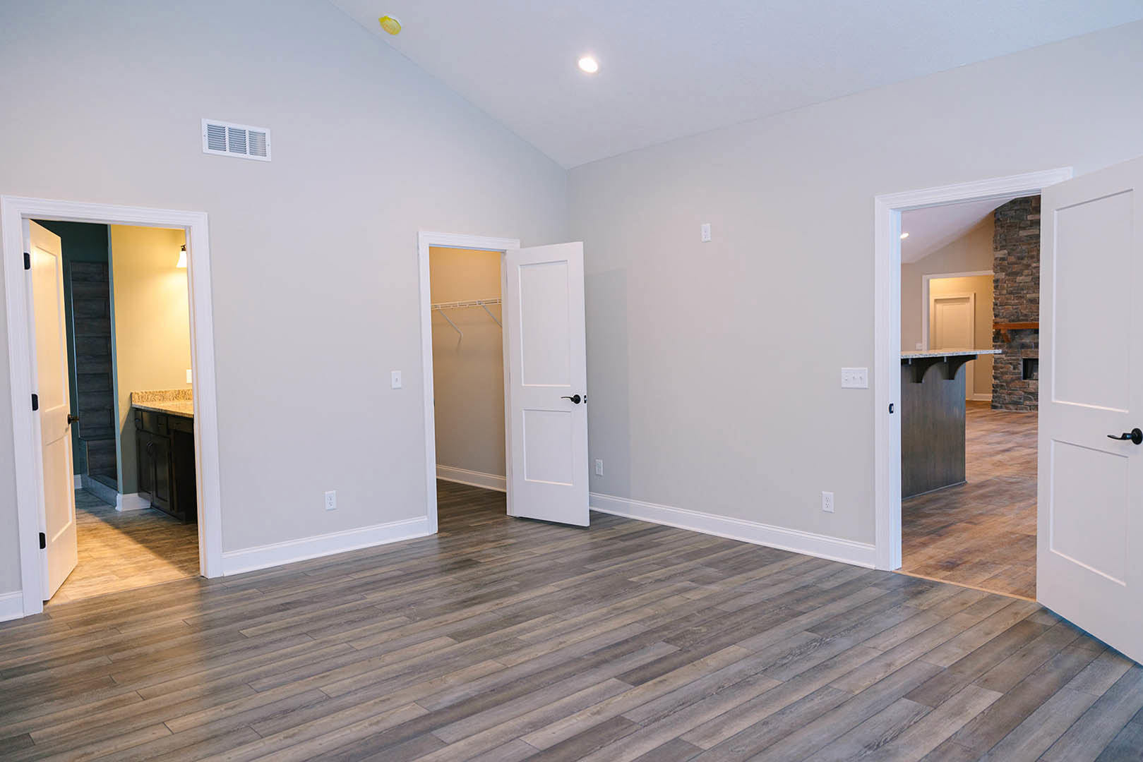 Wood flooring in a room with two open white doors, visible wall vent, cabinetry, and a white wire along the wall