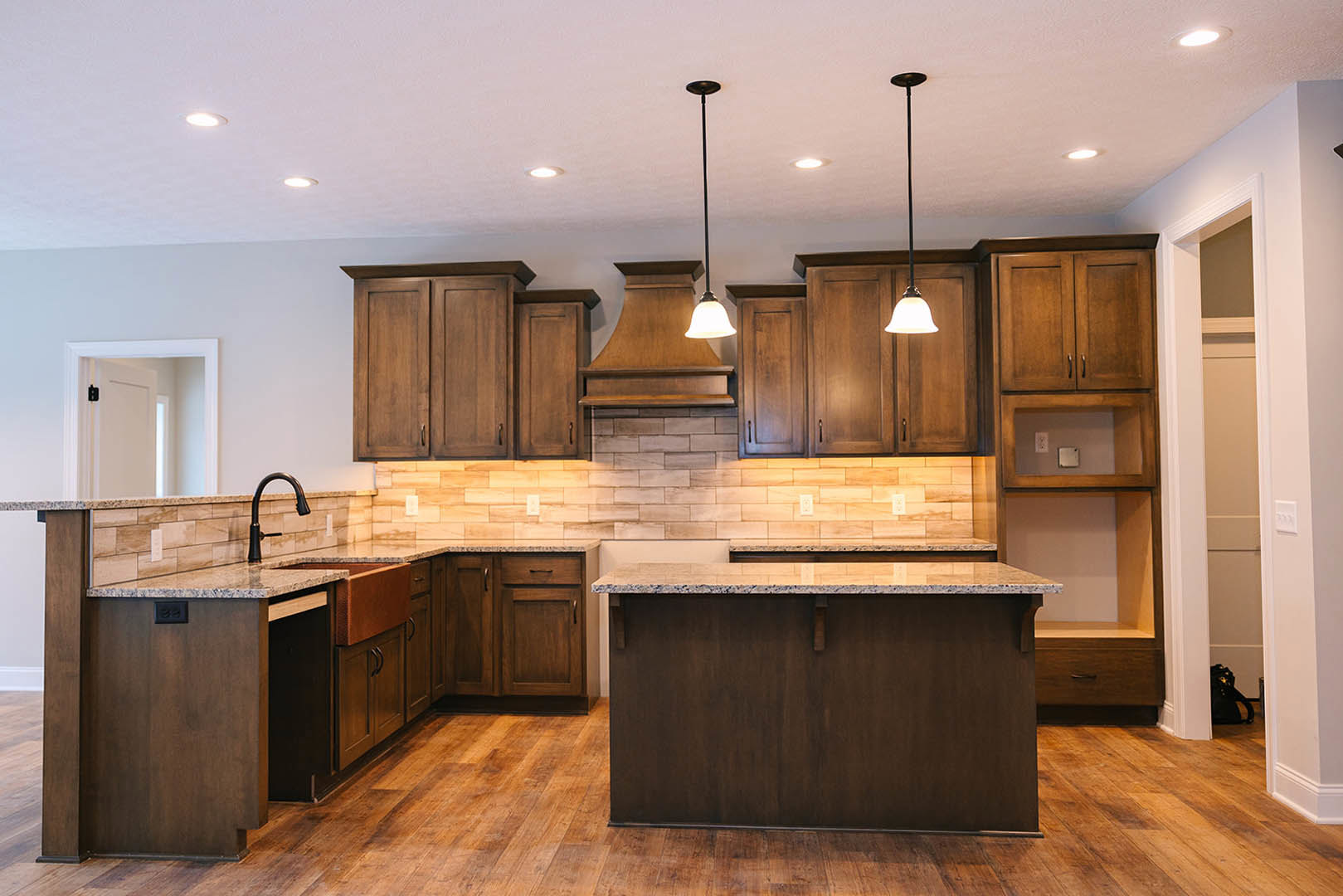Kitchen with wood cabinets, marbled countertop island featuring an inset sink, pendant lights suspended above, wood flooring, and a white door with black hardware.