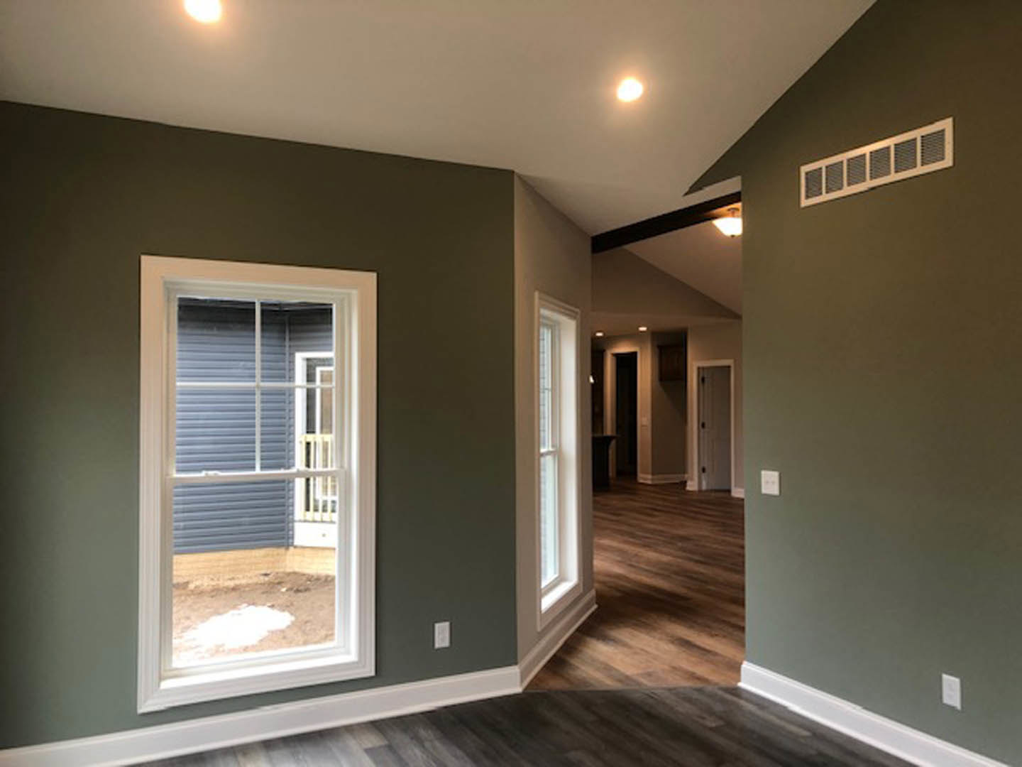 Sunlit room with white-framed window, wood laminate flooring, white baseboard trim, and wall vent visible near floor