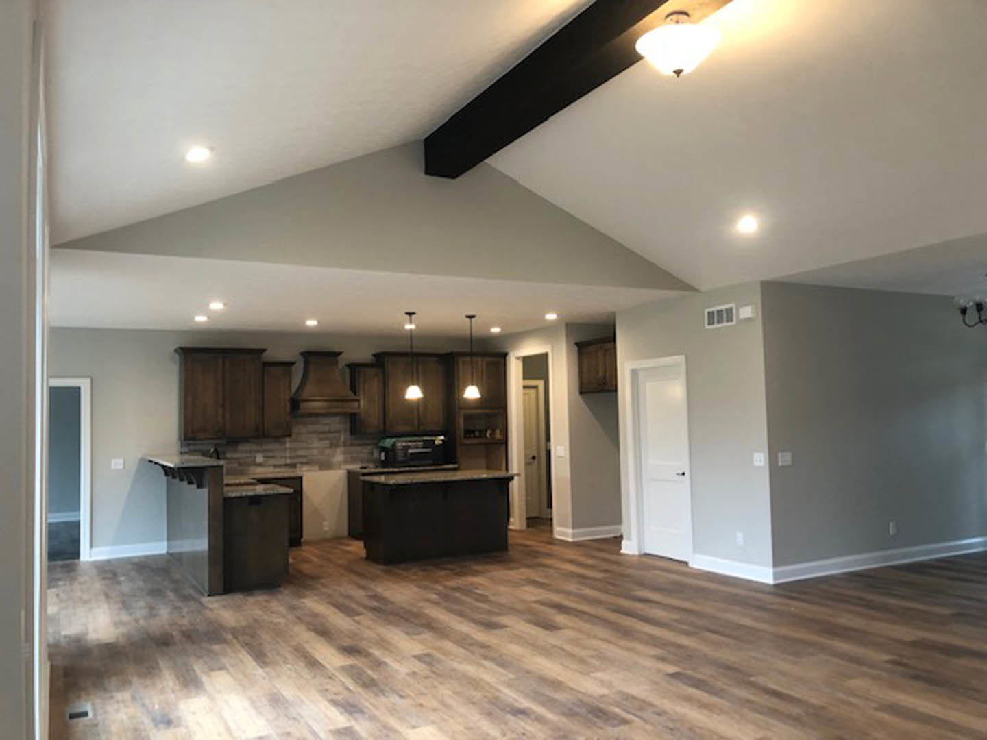 Open kitchen and dining area with hardwood floors, white walls, black dining table with wood top, modern cabinetry, and pendant light fixture.