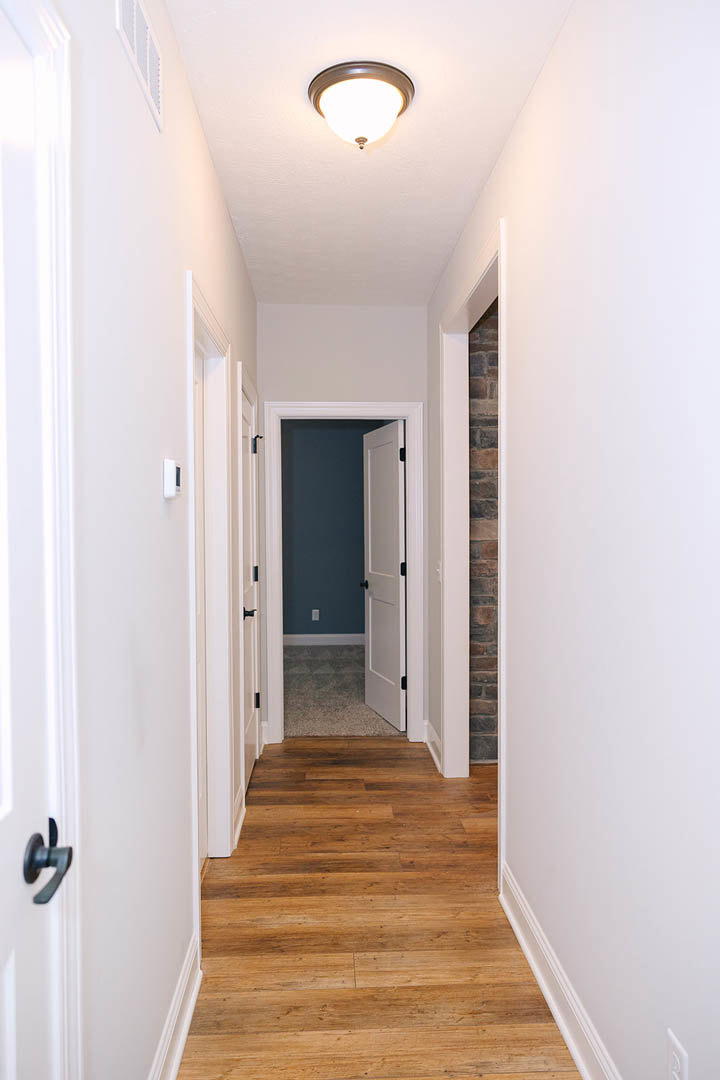 Hallway with white paneled doors, black door handles, light wood flooring, and smooth white plaster walls
