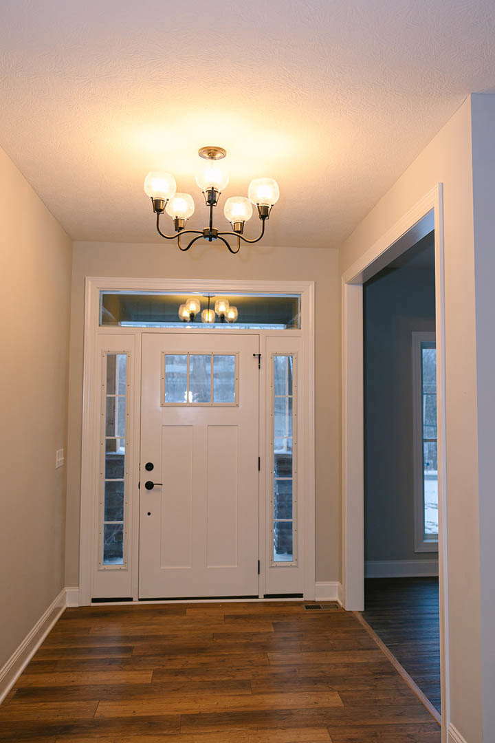 White door with glass windows, wood floor, multi-bulb ceiling light fixture, white window frame, interior wall molding