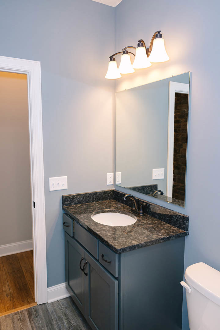 Bathroom with marble countertop, undermount sink, wall-mounted mirror, white light switch, chrome faucet, and tiled walls.