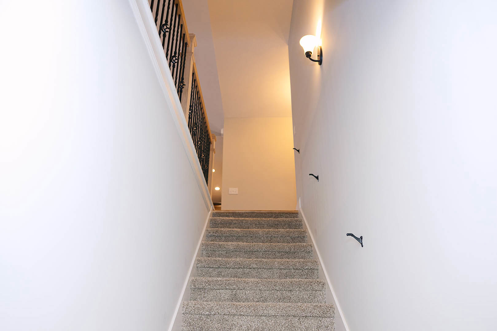Wood staircase with white plaster walls, modern wall-mounted light fixture, light hardwood flooring, and smooth ceiling.