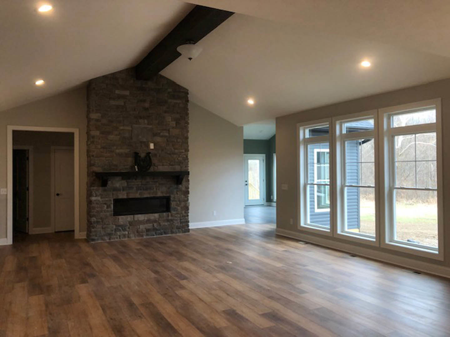 Living room with hardwood floors, white fireplace, multiple large windows, and a white door