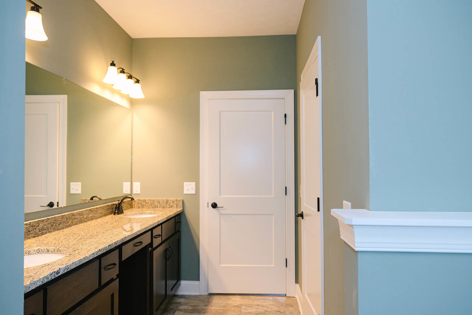 Bathroom featuring a white door with black handle, marble countertop, white cabinetry, wall-mounted light fixtures, and tiled walls.