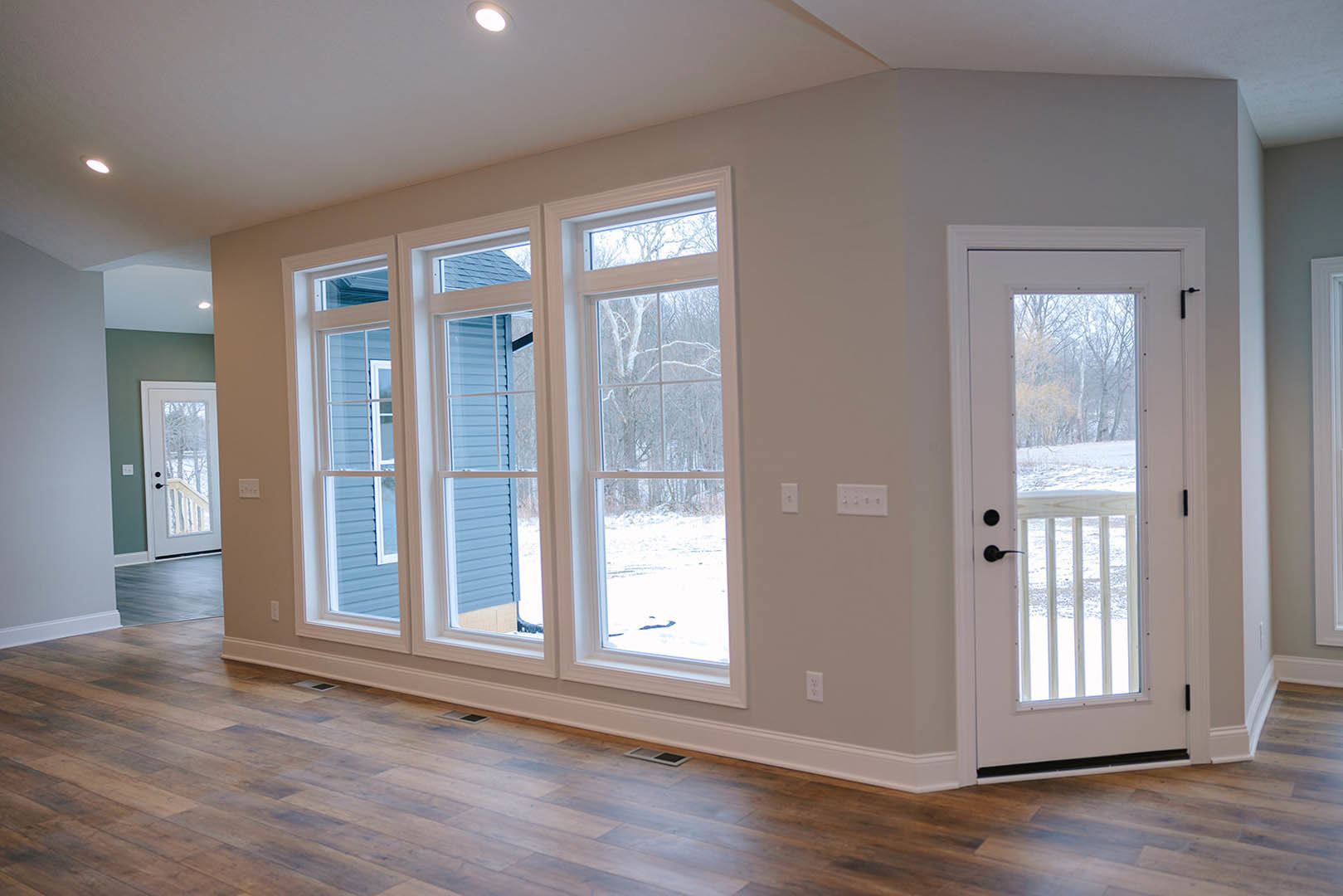 Wood-floored room featuring a frosted glass door, large windows overlooking snowy trees, and a central floor vent