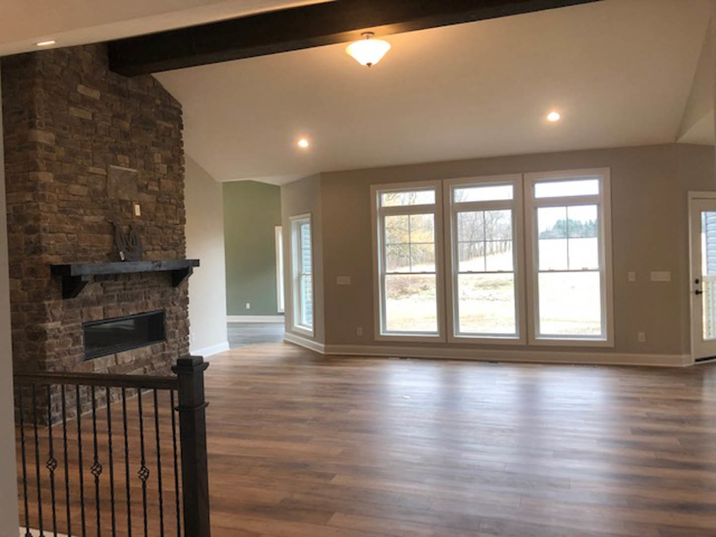 Living room with hardwood floors, stone fireplace, black metal railing, row of windows, glass doors, ceiling light fixture, and white molding