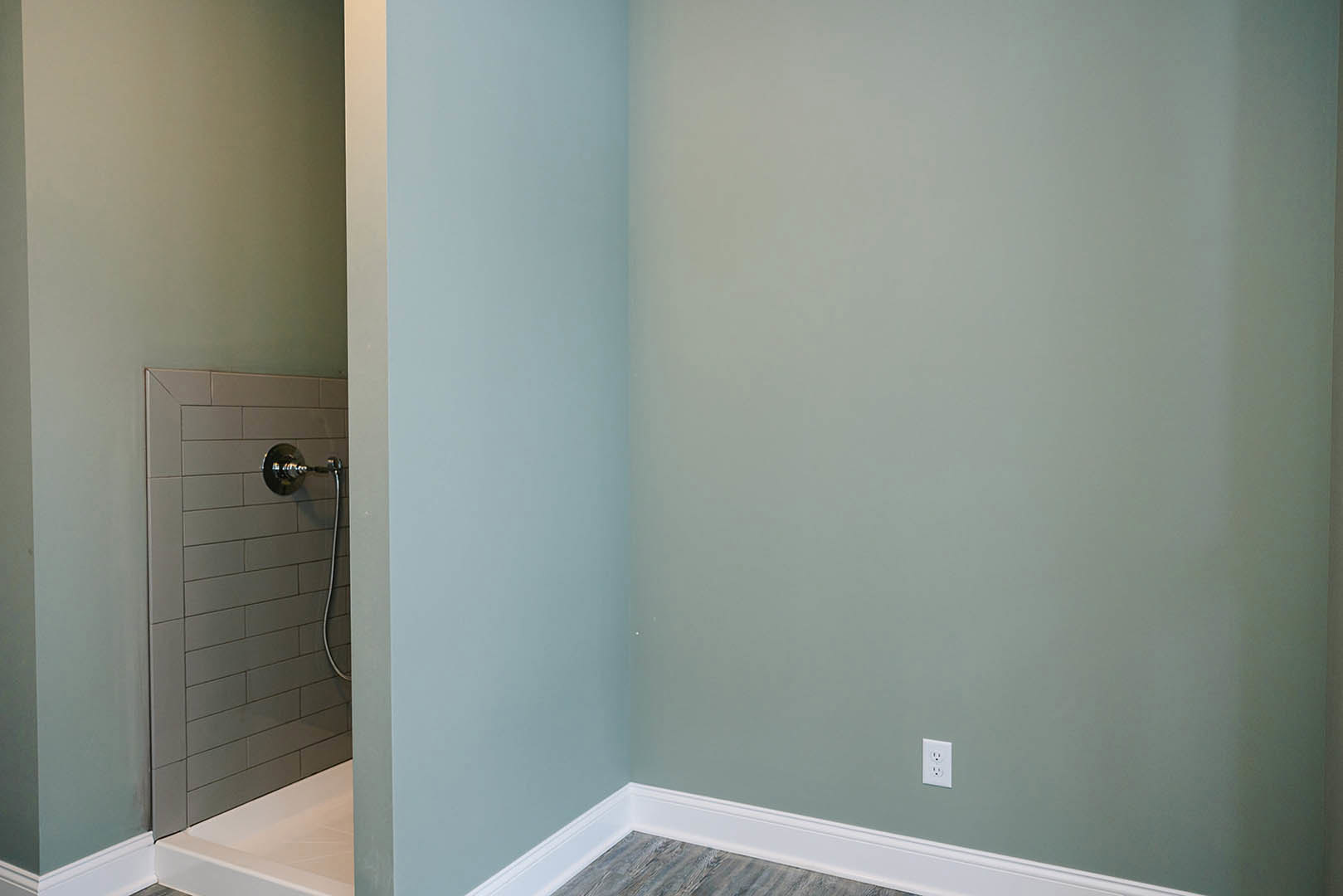 Walk-in shower with white tile walls, chrome shower head and hose, adjacent bathtub, white electrical outlet on wall, and modern light fixture