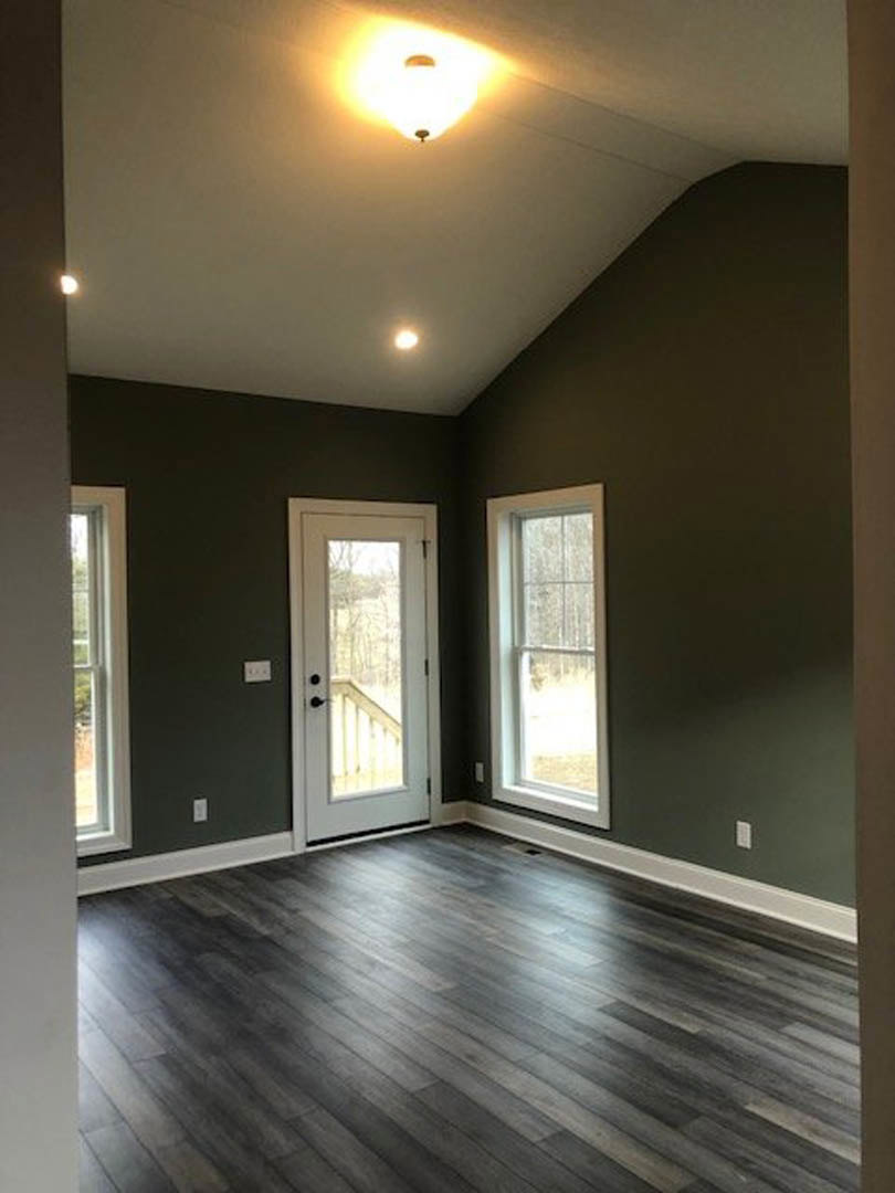 Dark wood flooring with white trim, white door with glass panel, two windows with white frames, light fixture illuminated, partial view of fence outside.