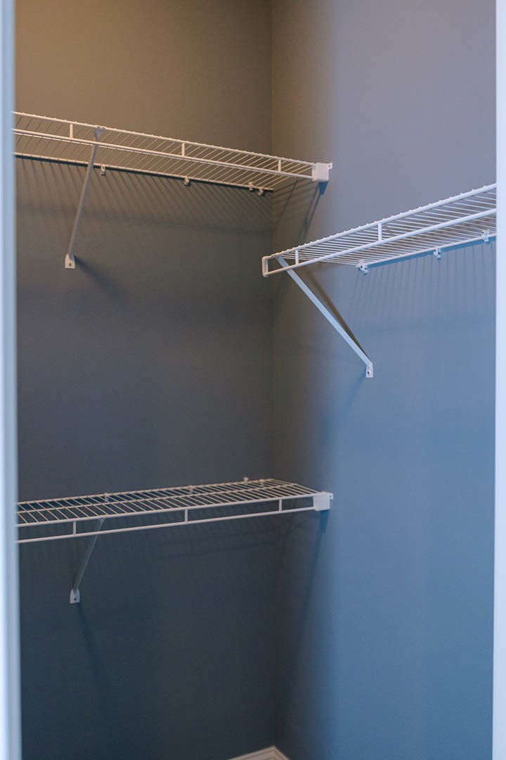 Walk-in closet with white wire shelving and hanging rod mounted on a blue accent wall