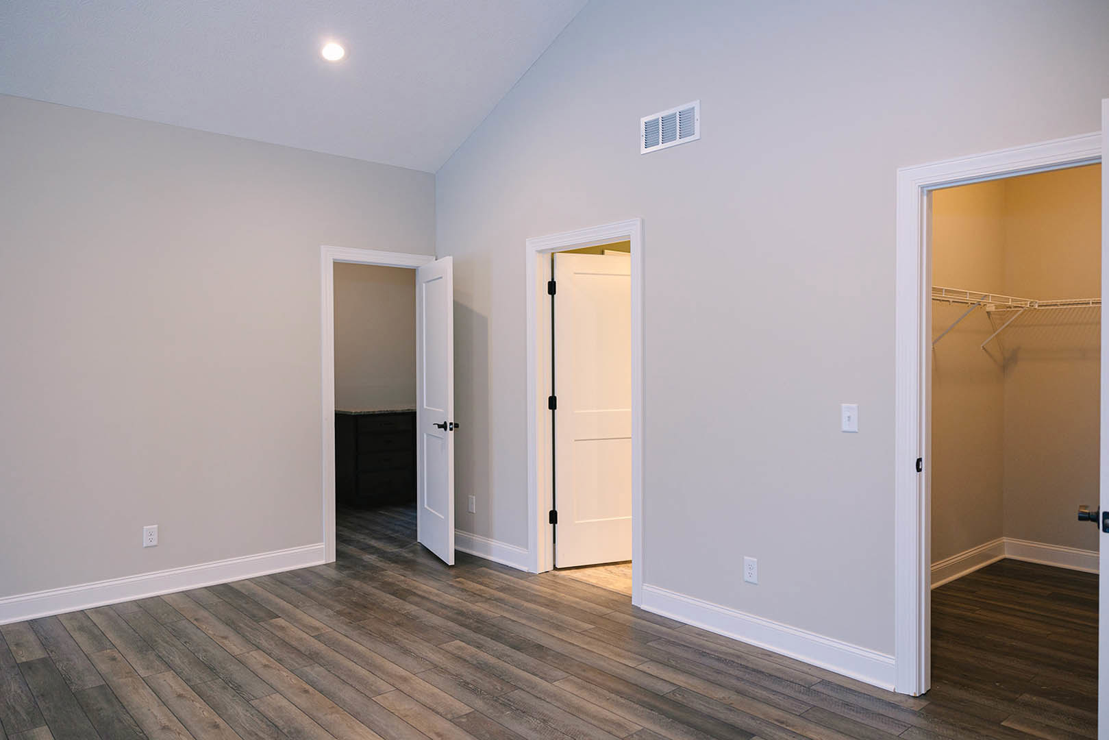White walls and wood flooring in a room with an open door, white vent, and closet featuring white shelves
