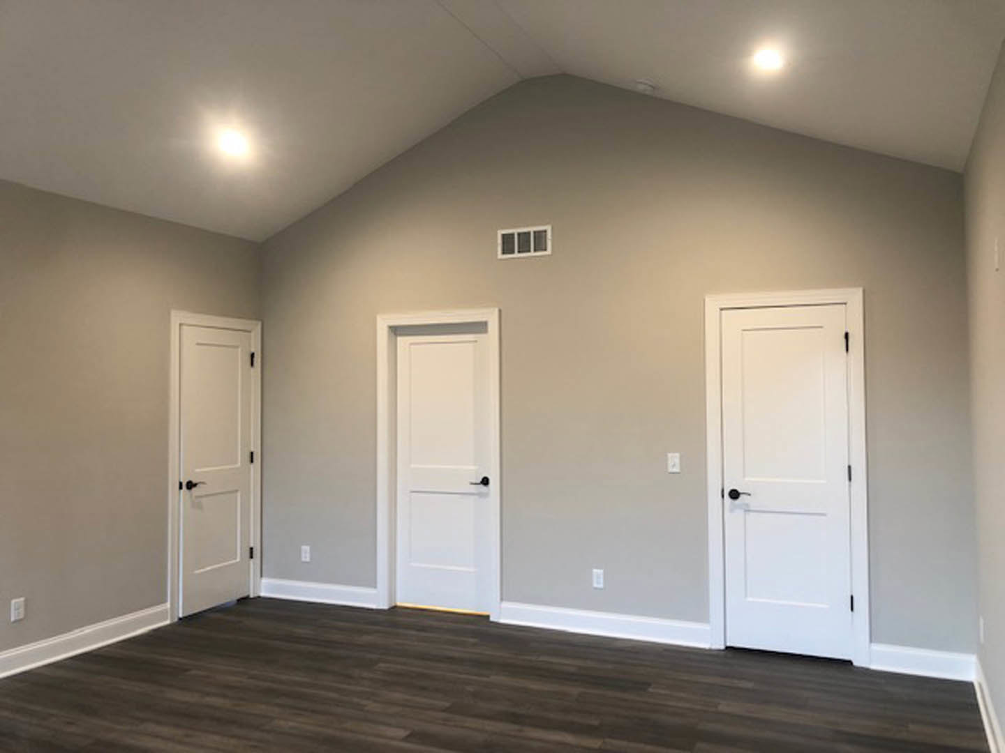 White paneled doors with black handles, dark wood flooring, white baseboards, and a square window in a bright interior room
