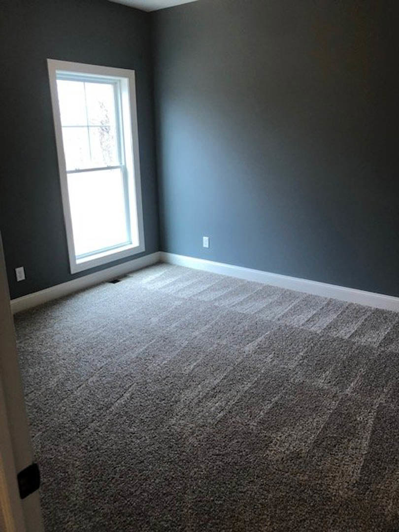 Carpeted bedroom with a large white-framed window, dark accent wall, and light grey walls