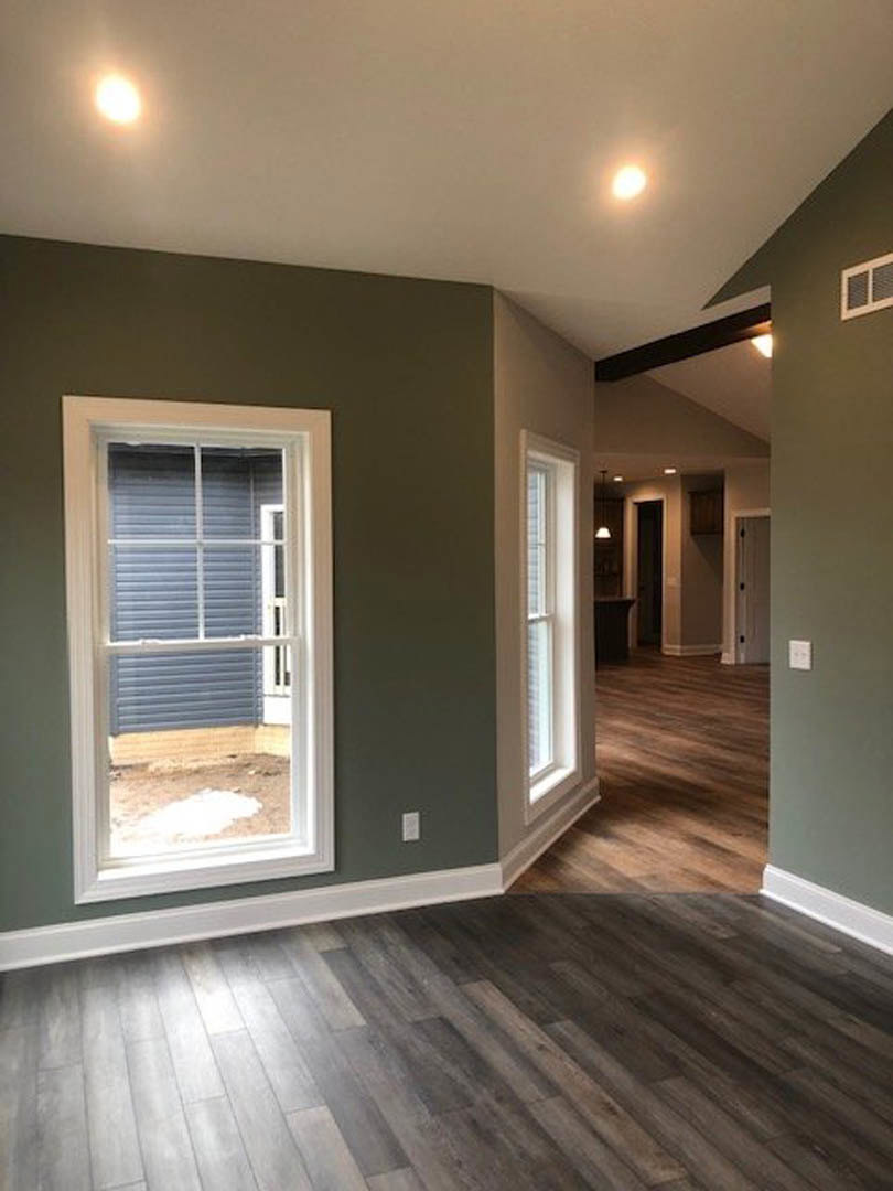 Sunlit room featuring a large window with white grid frame, wood flooring with white baseboard trim, and neutral walls.