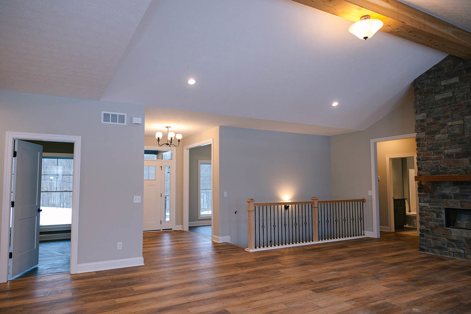 Open living area with hardwood floors, metal railing, white door with black handles, and modern chandelier