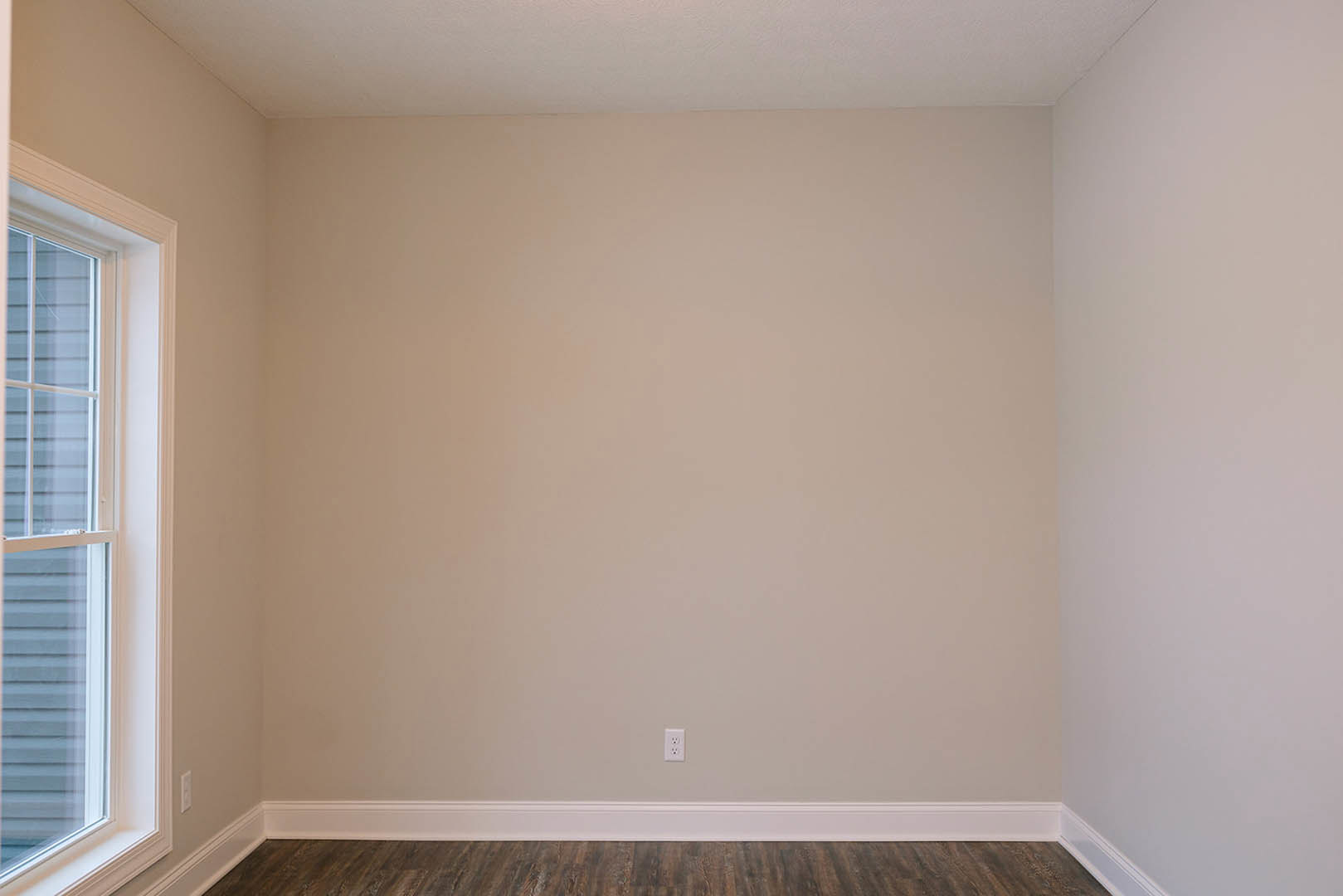 White-painted wall with white baseboard, wood plank flooring, window with white frame and blinds
