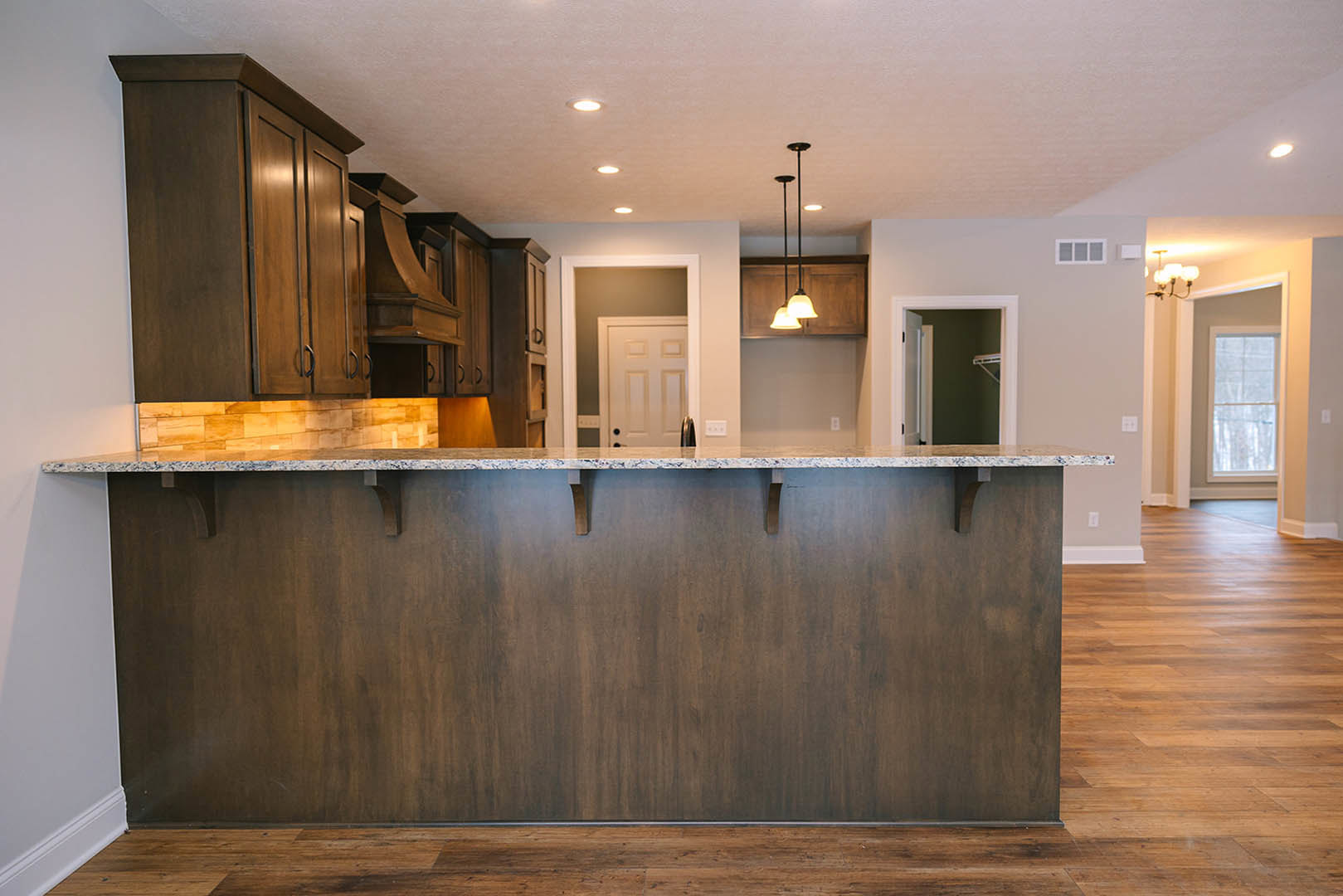 Modern kitchen with light wood flooring, white paneled door, white-framed window, sleek cabinetry, stone countertop, stainless steel sink, and metal bar stool