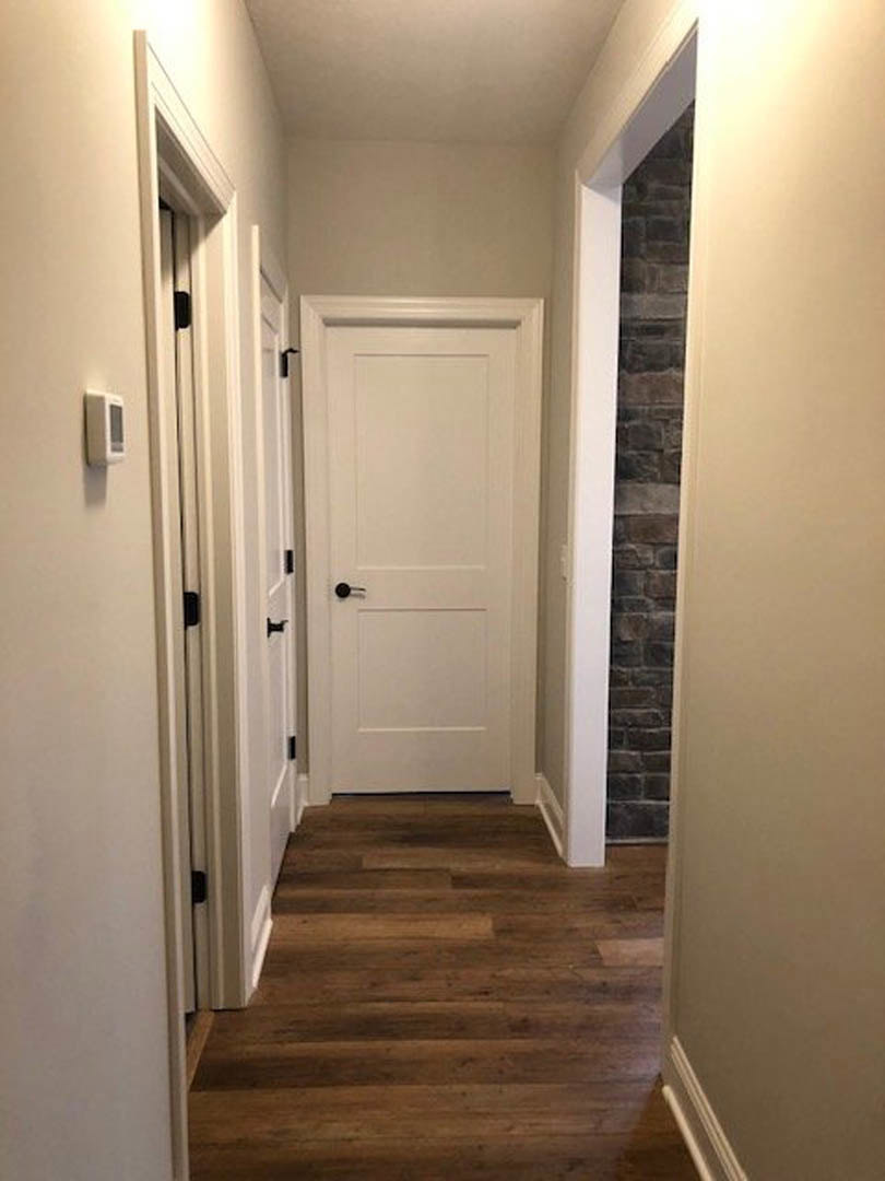 Hallway with light wood flooring, white doors featuring black handles, white baseboards, and smooth plaster walls