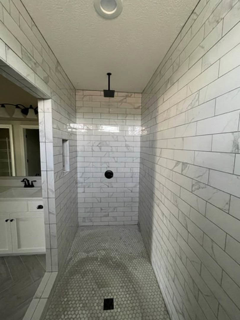 Marble tile shower with glass enclosure, wall-mounted sink, chrome shower head, and recessed lighting on white ceiling