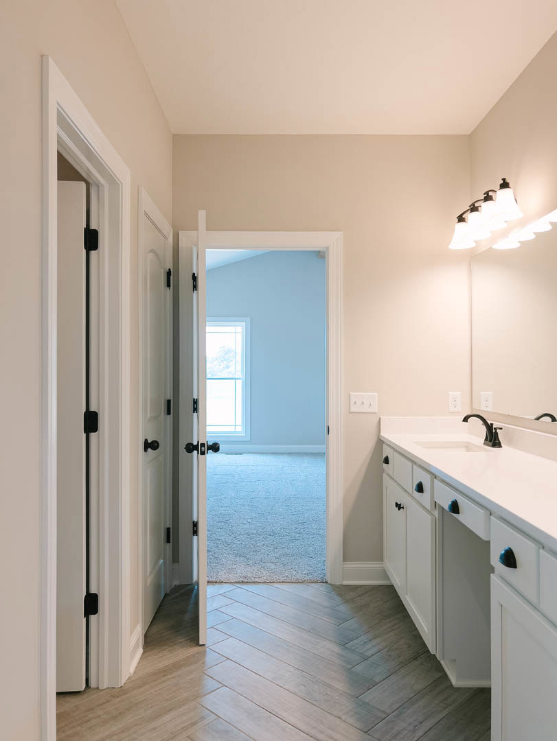 Bathroom with white rectangular sink, wood plank flooring, white door with black hardware, wall-mounted row of lights, window framed in blue.