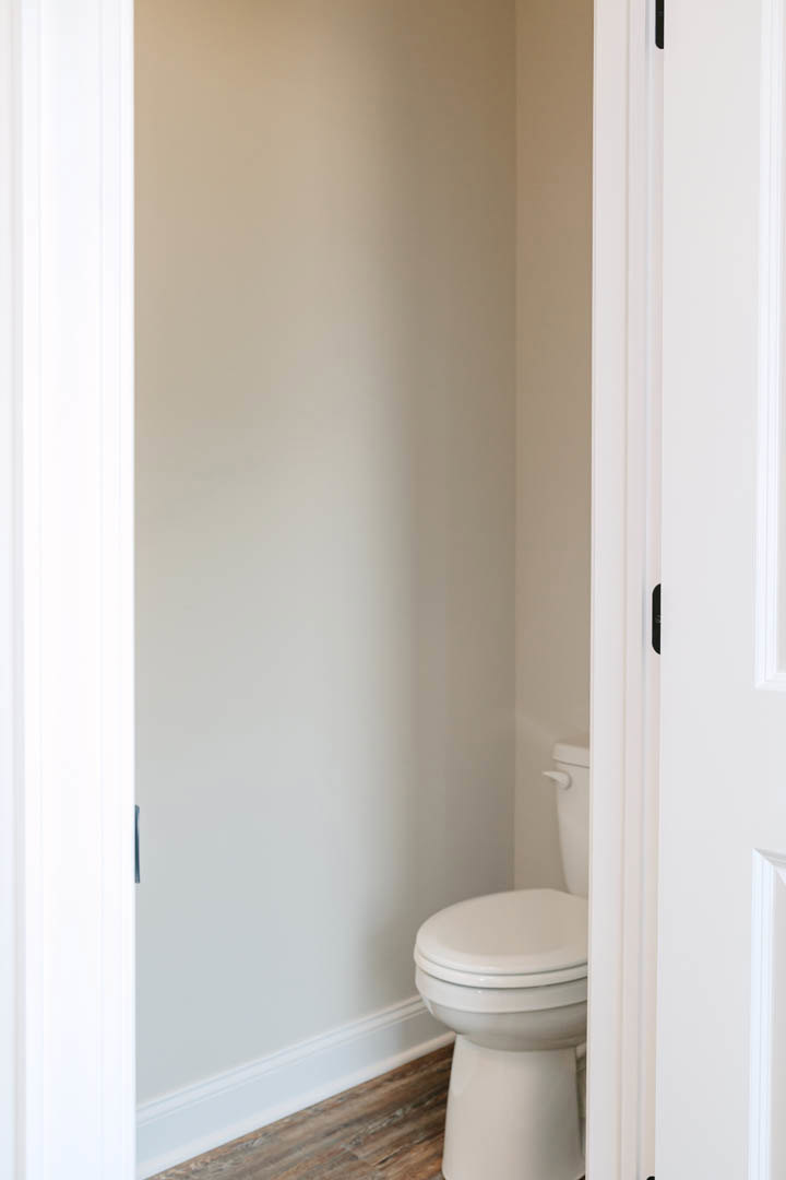 White toilet with closed seat on wood flooring, white baseboard, and white wall with black trim in a bathroom.