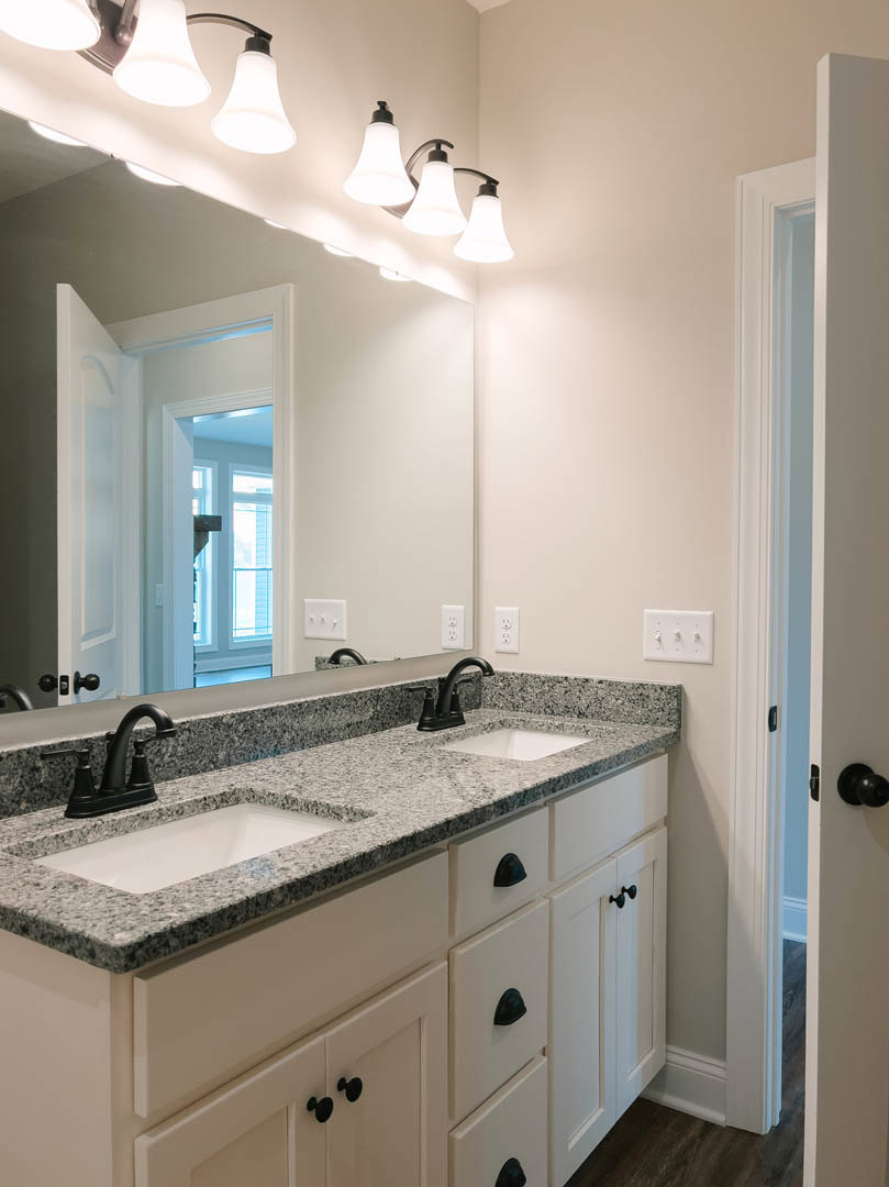 Marble bathroom countertop with black faucet, white sink, wall-mounted mirror, white light switch with knobs, and close-up of light fixture above tile backsplash