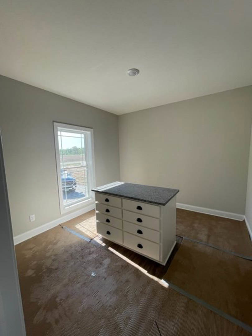 White cabinetry with black handles beneath a light-colored countertop, laminate flooring, large window with partial view of a parked car outside, smooth plaster walls, and white