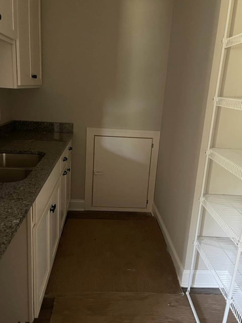 Modern kitchen featuring white cabinetry, stainless steel appliances, brown wood flooring, a small white door with a handle, and open shelving against a white wall.