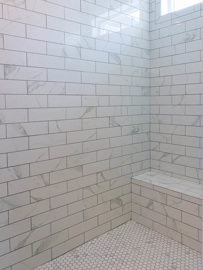 White tile shower with black grout, built-in bench, and white tile floor featuring black hexagon accents